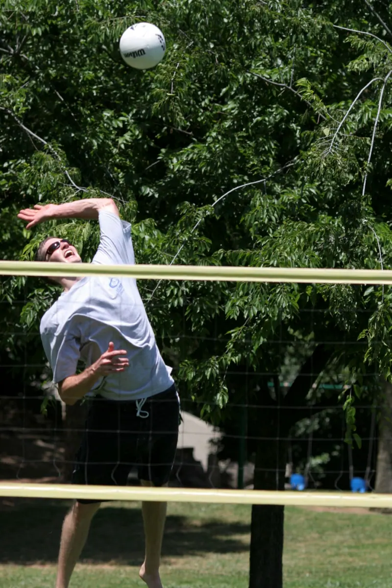 Jogador de vôlei cortando a bola na rede, braço no alto